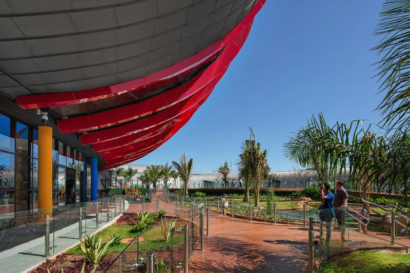 Covered outdoor terrace with red curved canopy above water features and palm plantings