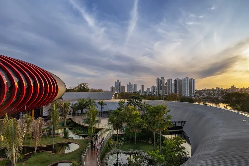 Aerial view of ribbed roofing volumes and landscaped grounds with palms against a distant skyline at sunset