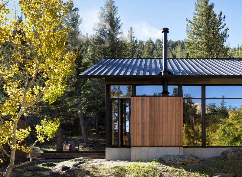 Exterior view showing standing seam metal roof, timber and glass facade, and concrete plinth among aspens