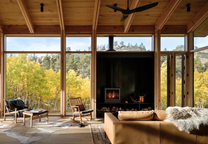 Living room with black steel fireplace surround framed by full-height windows overlooking yellow-leaved aspens