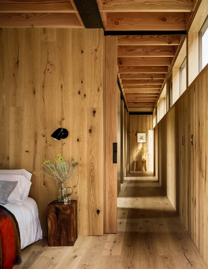 Narrow timber-clad hallway with exposed ceiling joists and afternoon sunlight filtering through the corridor