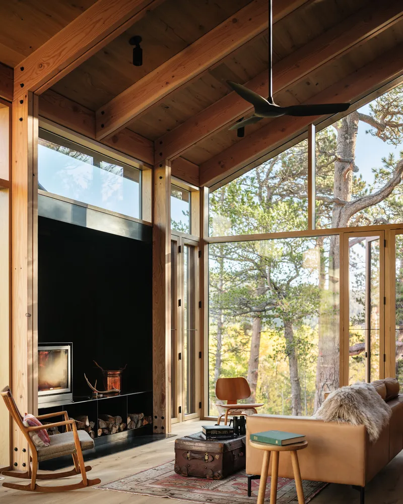 Living room with exposed timber ceiling beams and floor-to-ceiling glass overlooking autumn aspens