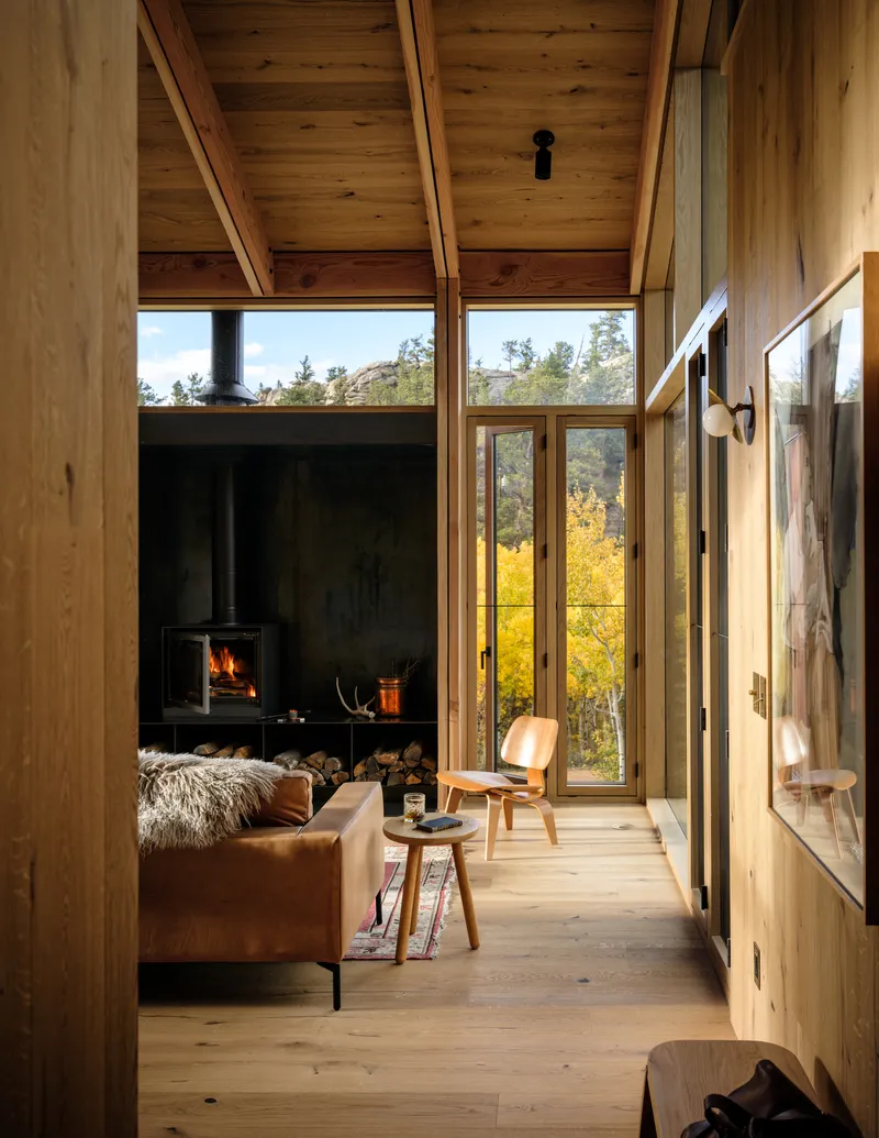 Wood-lined interior corridor with black steel fireplace surround and view to golden foliage
