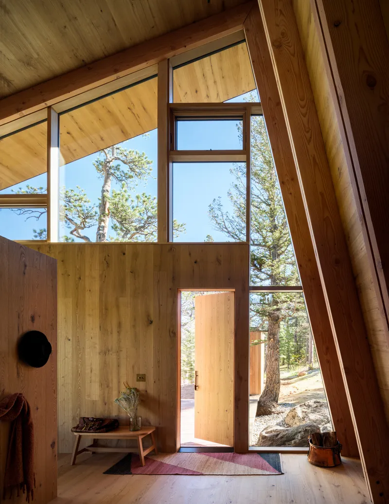 Double-height entryway with angled timber-framed glazing and open door to the forest