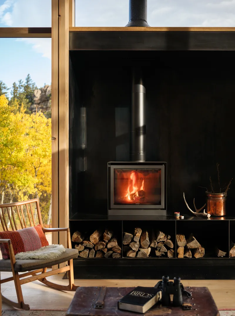 Freestanding wood stove on black steel base with firewood storage and view to yellow aspens