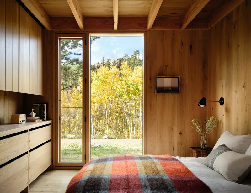 Timber-lined bedroom with exposed beam ceiling and full-height glazing framing golden aspen trees in autumn