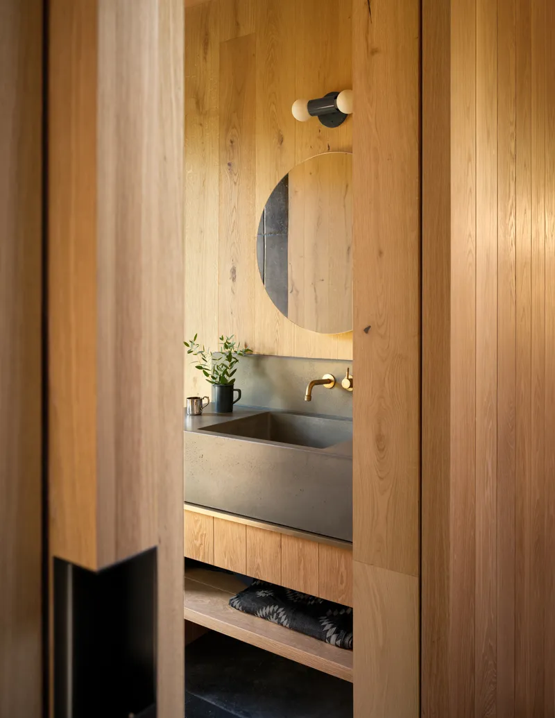 View through timber doorway to bathroom vanity with concrete counter and circular mirror above