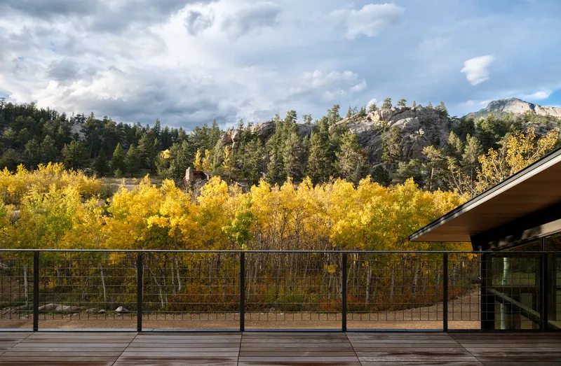 Exterior deck with cable railing overlooking autumn aspens and forested mountains under dramatic clouds