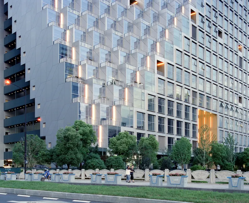 Ground-level view showing the modular facade above a row of planters and pedestrians at twilight