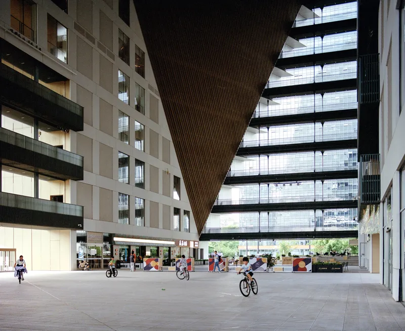 Covered courtyard beneath a triangular slatted ceiling with cyclists passing through the open plaza
