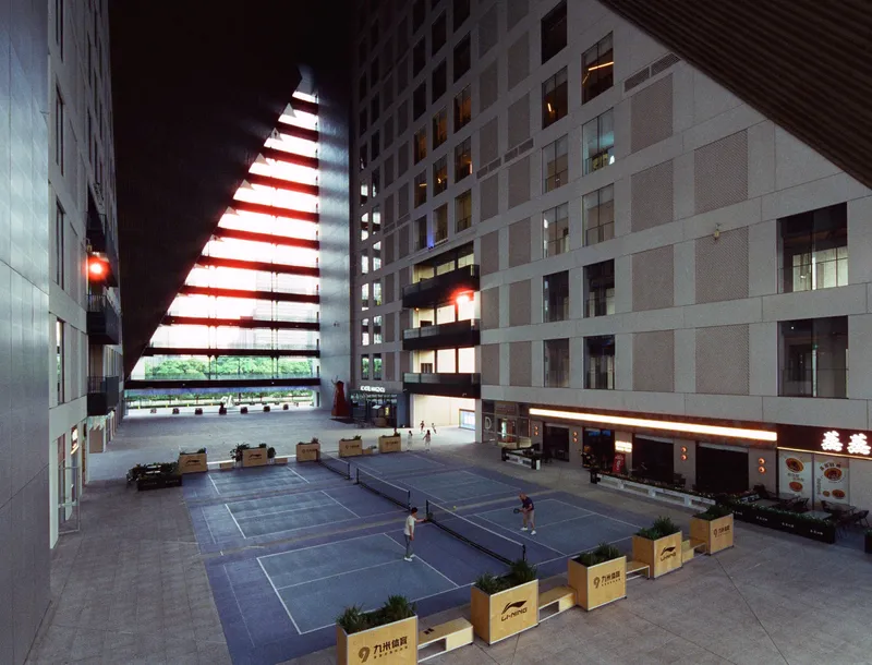 Nighttime courtyard with illuminated triangular opening and wooden seating boxes on the paved plaza