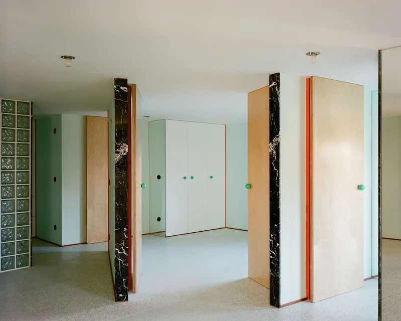 Interior space with pale-wood and black marble-clad doors, glass block wall, and turquoise door handles