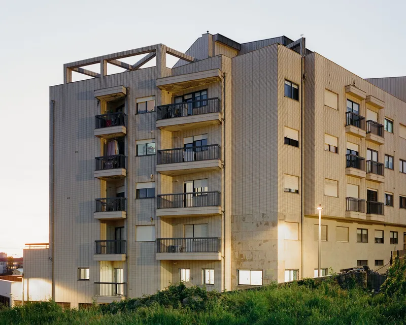 Facade of a multistory residential block with corrugated metal cladding and recessed balconies at dusk