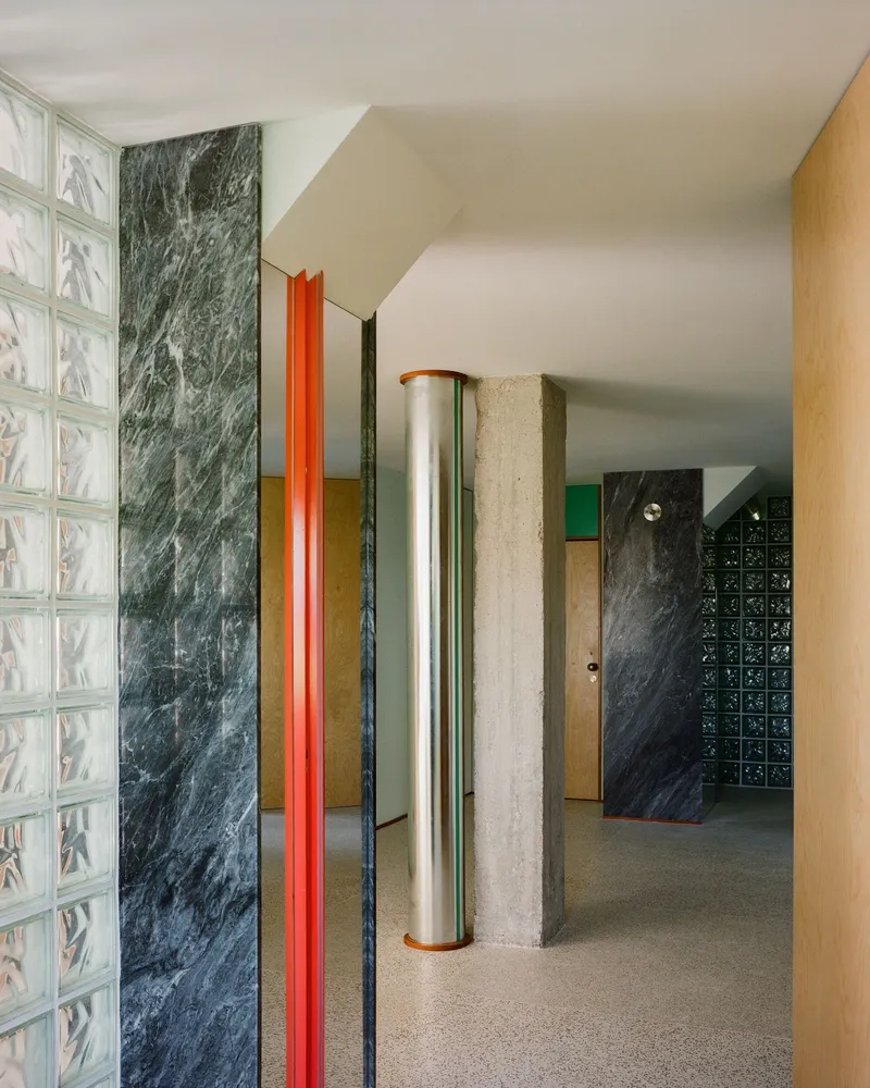 Entry hall with glass block wall, dark marble panels, orange metal trim, and cylindrical columns