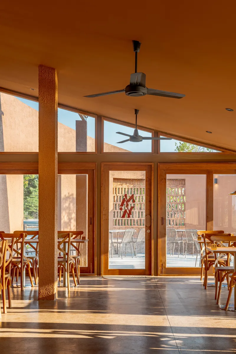 Interior dining space with timber-framed glazing and ceiling fans beneath a sloped ceiling in sunlight