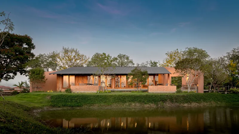 Illuminated timber and brick facade reflected in pond at twilight beneath a dark metal roof