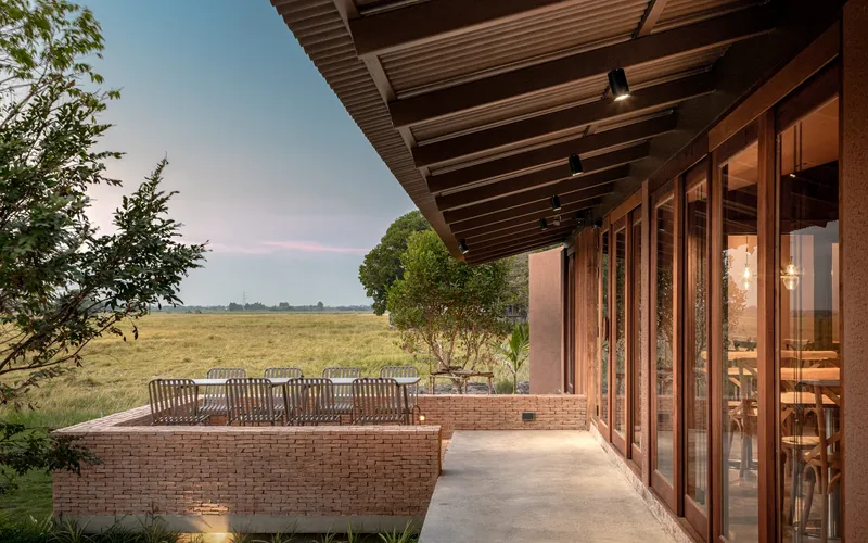 Deep overhang with exposed rafters sheltering timber-framed glazing and brick seating wall facing open fields