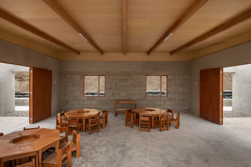 Interior space with exposed timber ceiling beams and round wooden tables beneath block wall windows