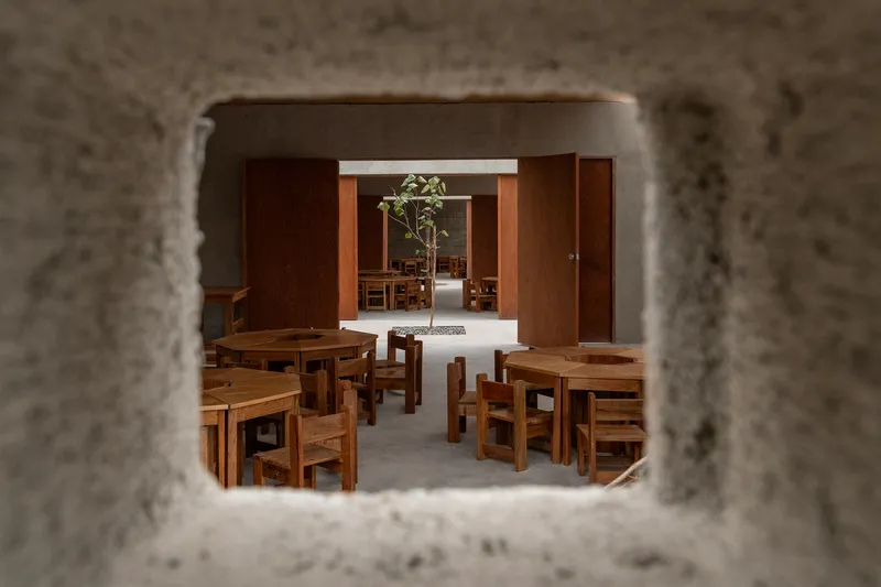 View through concrete block window opening to timber furniture and aligned doorways beyond
