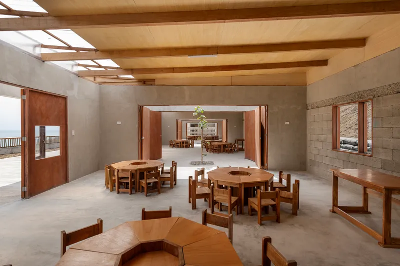 Interior dining hall with exposed timber beams, concrete block walls, and wooden furniture arranged under skylights