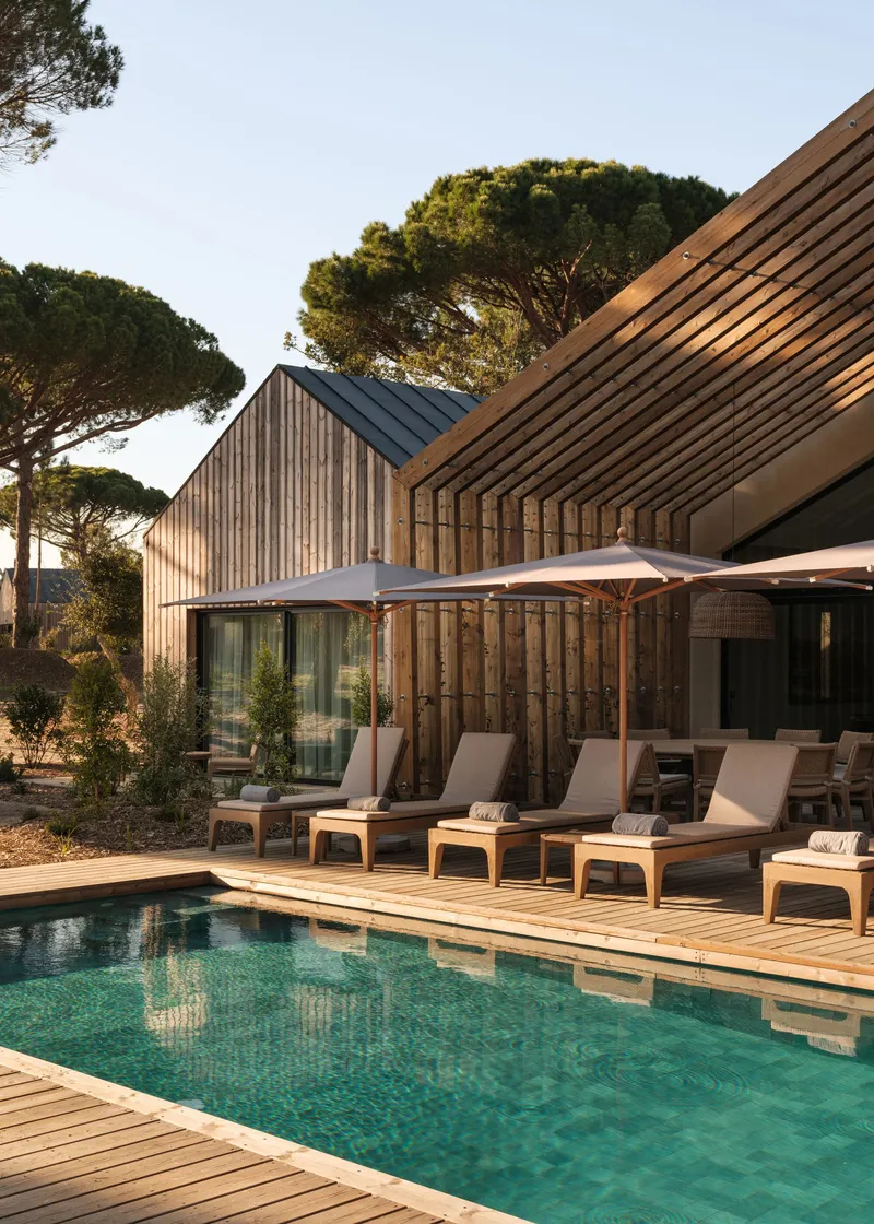 Timber deck with lounge chairs and white umbrella alongside the pool at dusk beneath the vertical-clad gables