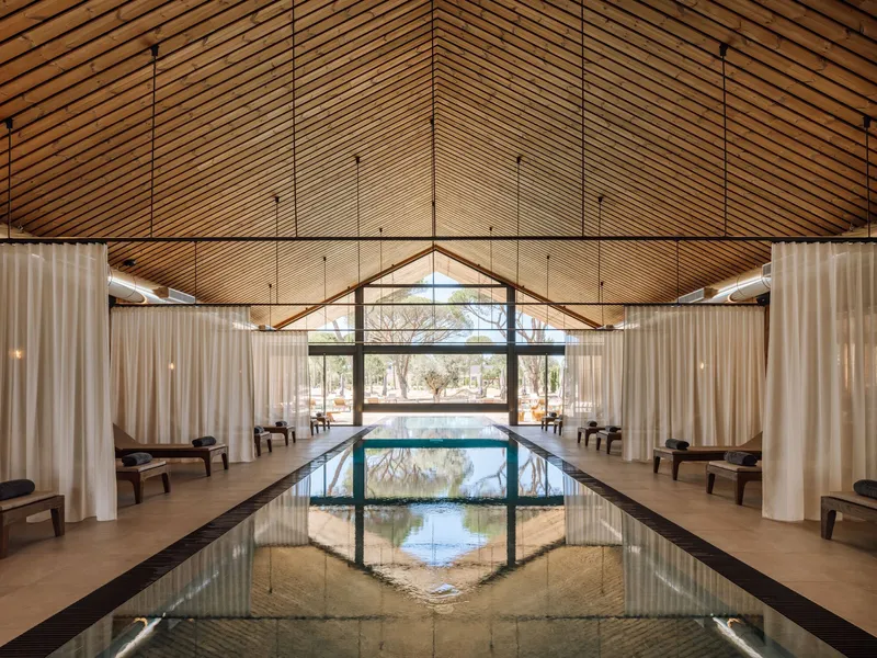 Interior lap pool under a gabled wood slat ceiling with white curtains flanking the lounging alcoves