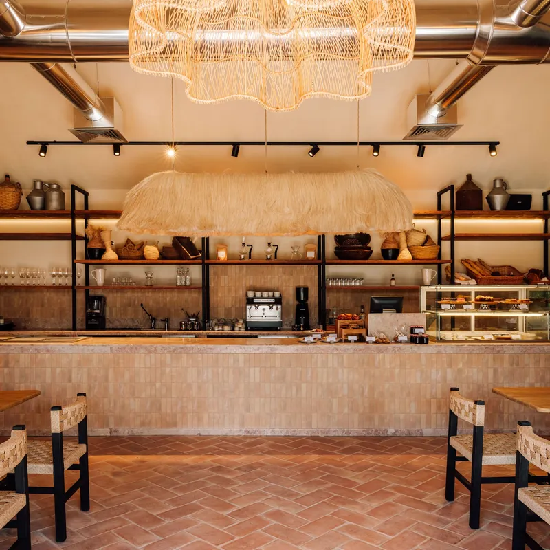 Service counter with mosaic tile front, woven pendant lights and open shelving displaying ceramics