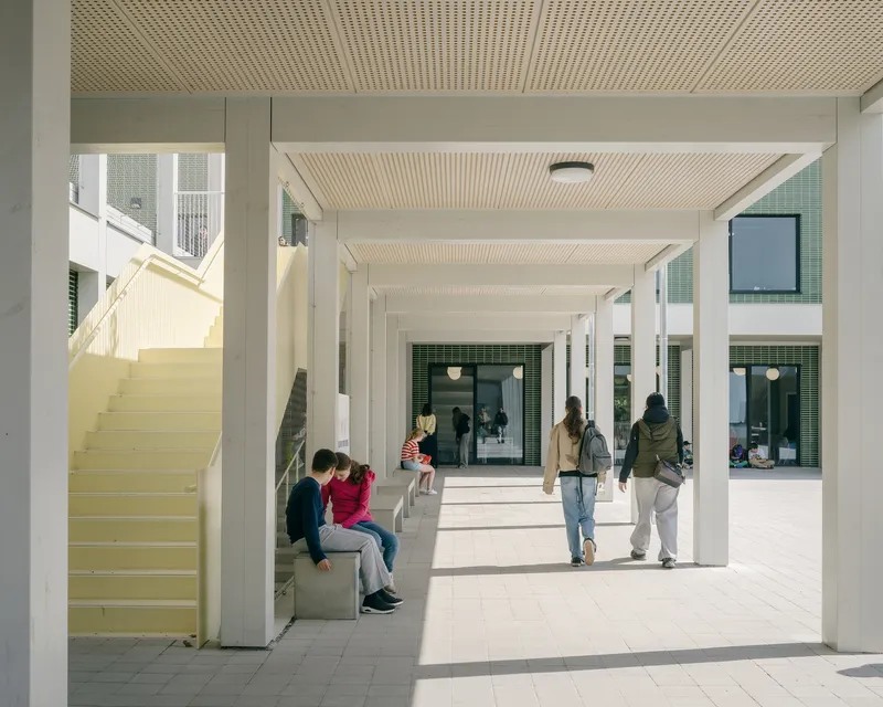 Covered walkway with exposed timber slat ceiling and concrete columns as students gather