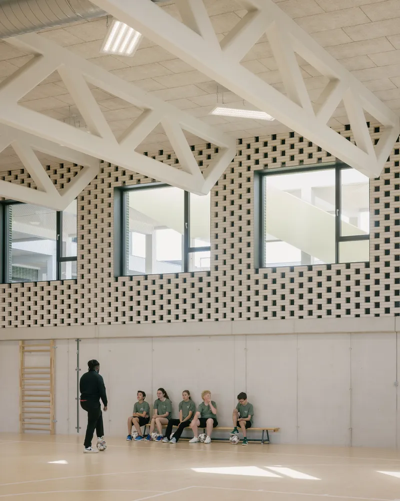 Gymnasium with exposed white timber trusses and chequered brick upper wall where students sit
