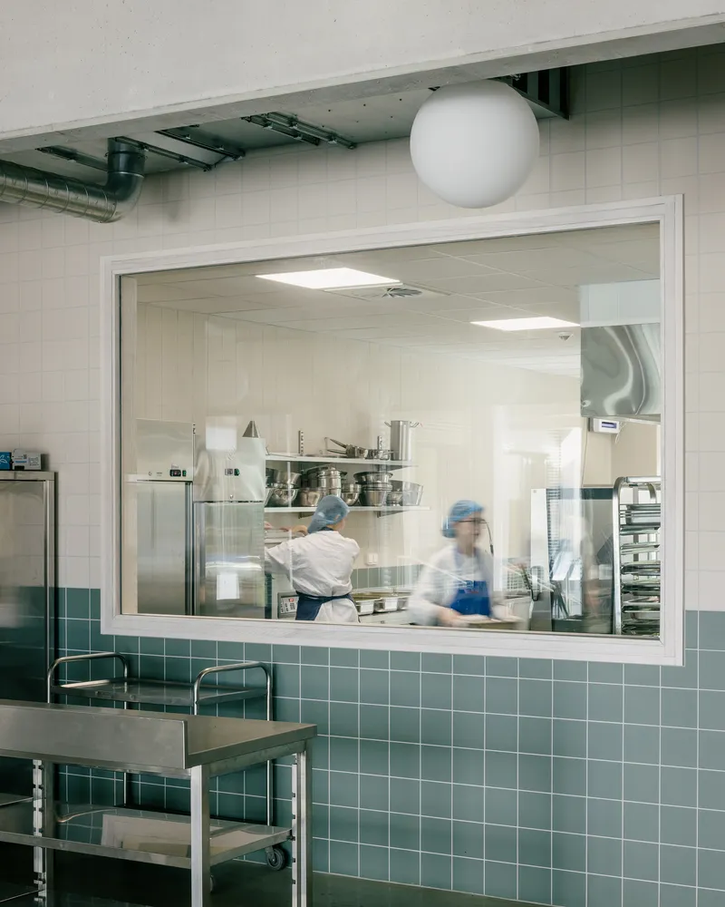 Kitchen pass-through window framed in white with teal tile surround and workers in motion