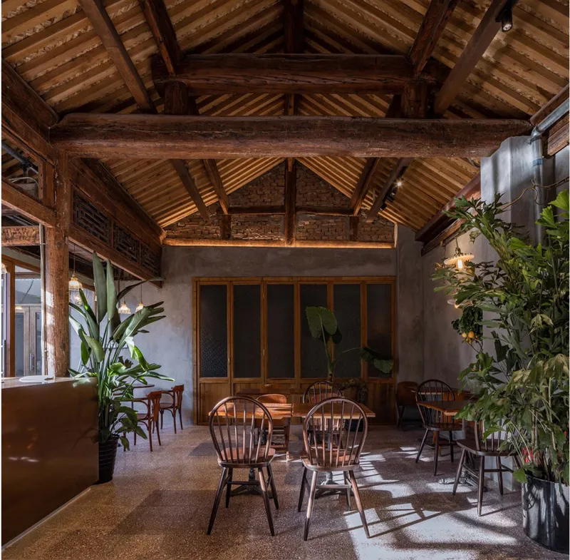 Warm café seating framed by exposed timber trusses, brick walls, and indoor greenery.