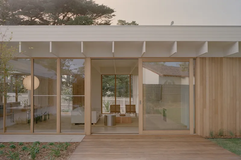 Facade with floor-to-ceiling glazing and exposed beam overhang framing views to planted courtyard