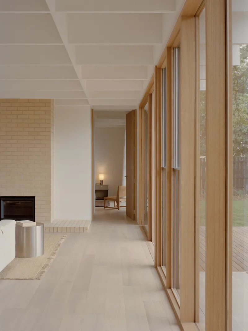 Corridor with floor-to-ceiling timber-framed glazing overlooking garden at dusk