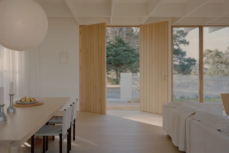 Living and dining space with oak-clad sliding doors opening to pine trees outside