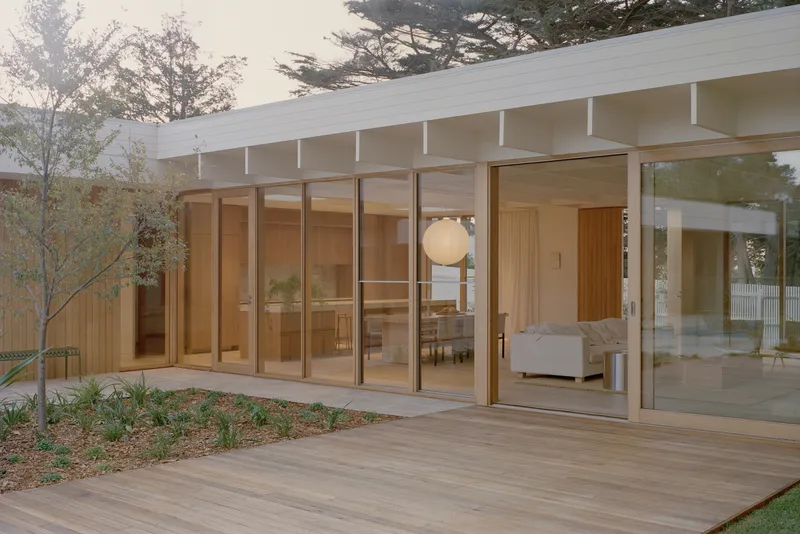 Timber deck extending from floor-to-ceiling glass doors with planted bed along the side