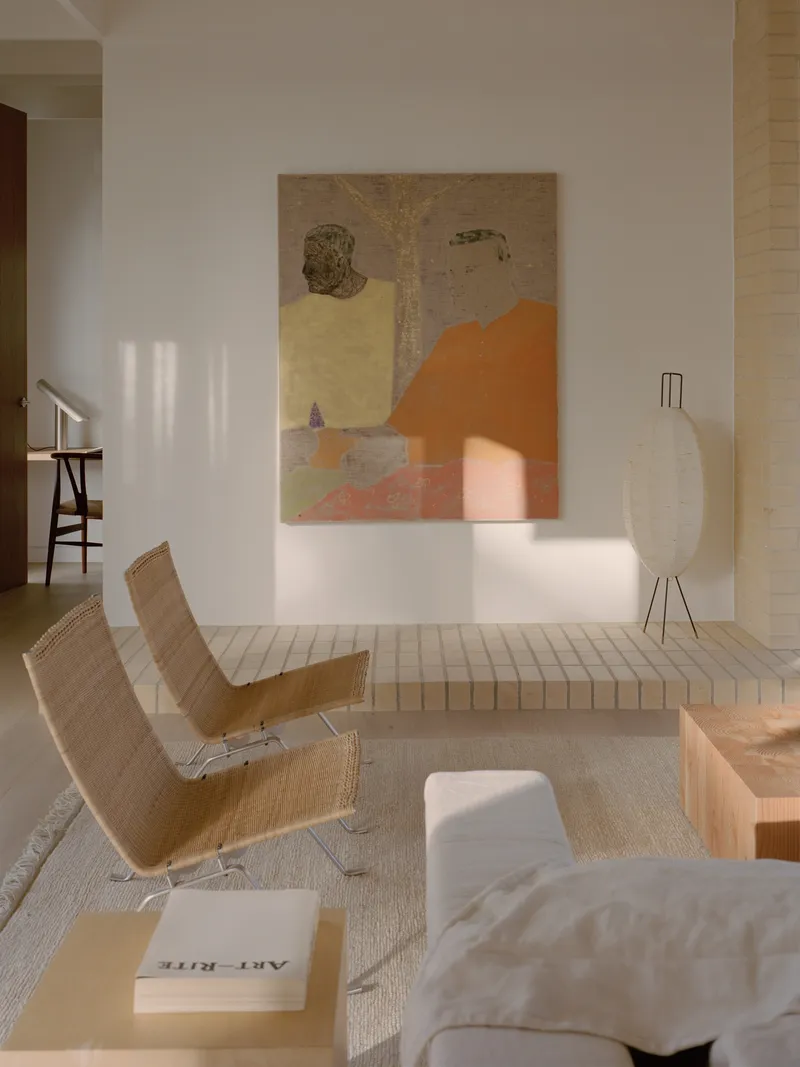 Living area with woven lounge chairs and artwork illuminated by afternoon sunlight