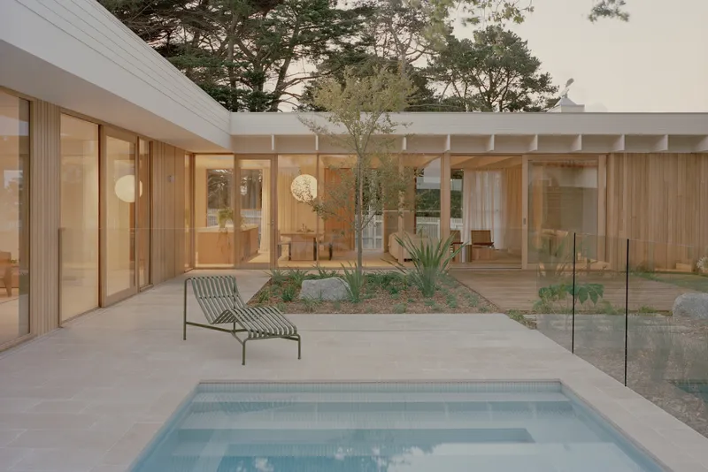 Courtyard pool with glass fencing and planted bed surrounded by timber framed glazing at dusk