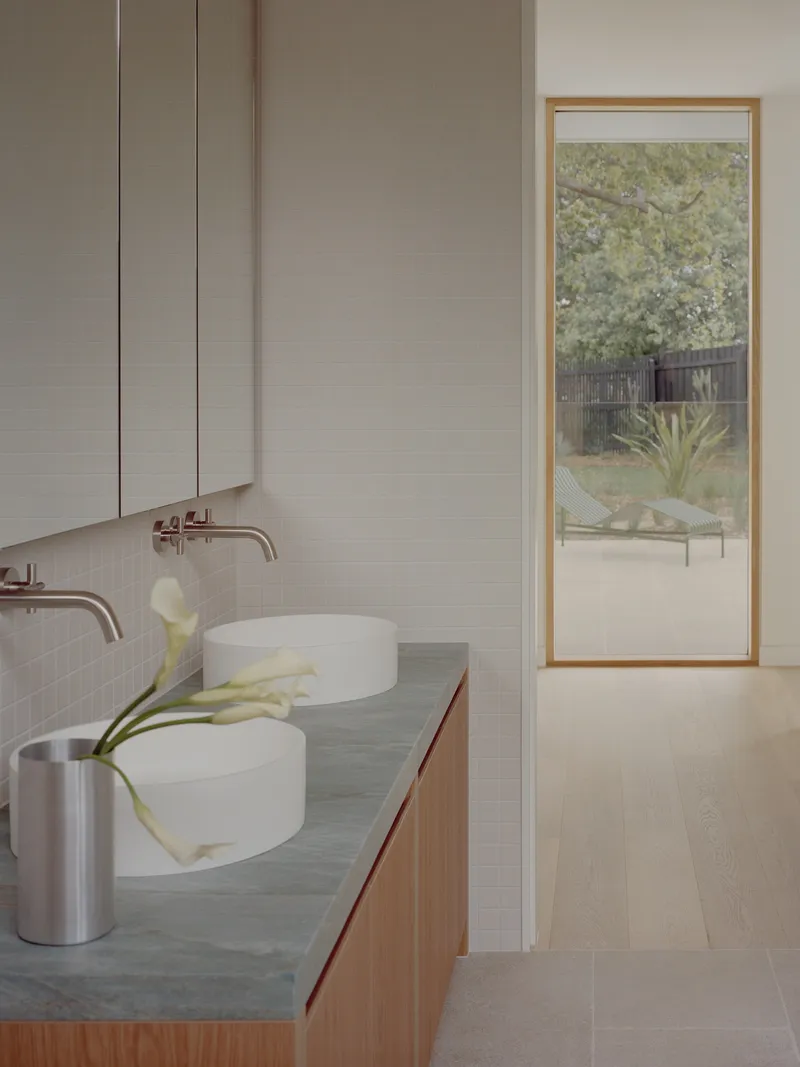Bathroom vanity with twin vessel sinks and timber-framed window overlooking a garden courtyard