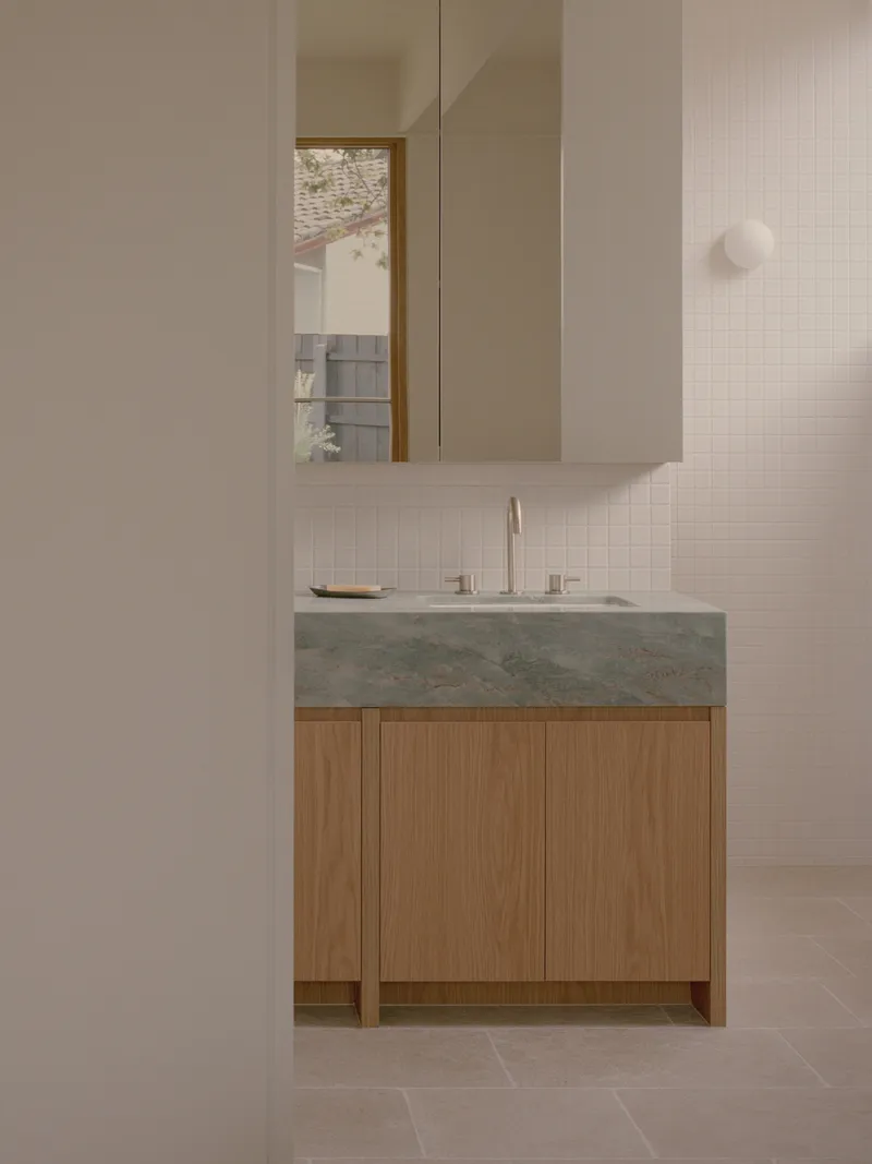 Floating oak vanity with integrated green stone counter below white wall cabinets and medicine mirror