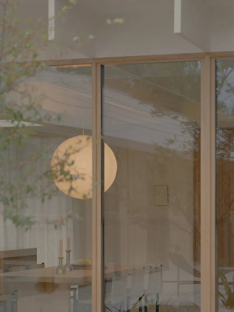 View through timber-framed glass doors with spherical pendant light and garden foliage beyond
