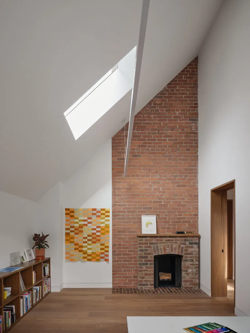 Exposed brick fireplace beneath a sloped ceiling with angled skylight illuminating the chimney wall