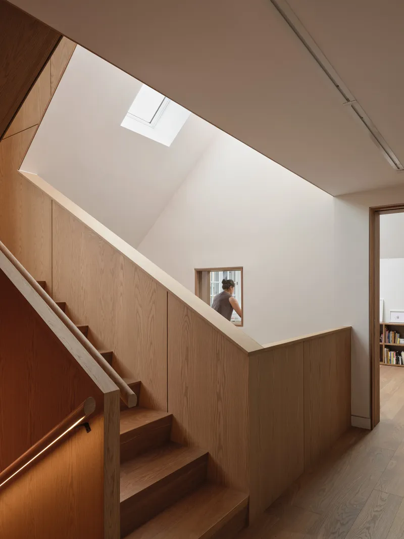 Timber-clad stairwell with skylight above and figure visible through a rectangular wall opening