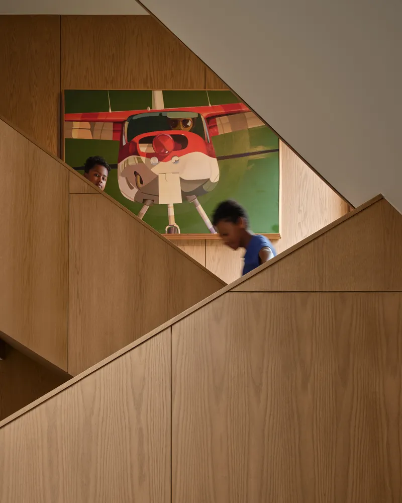 Wood staircase with two children ascending beneath a large figurative painting