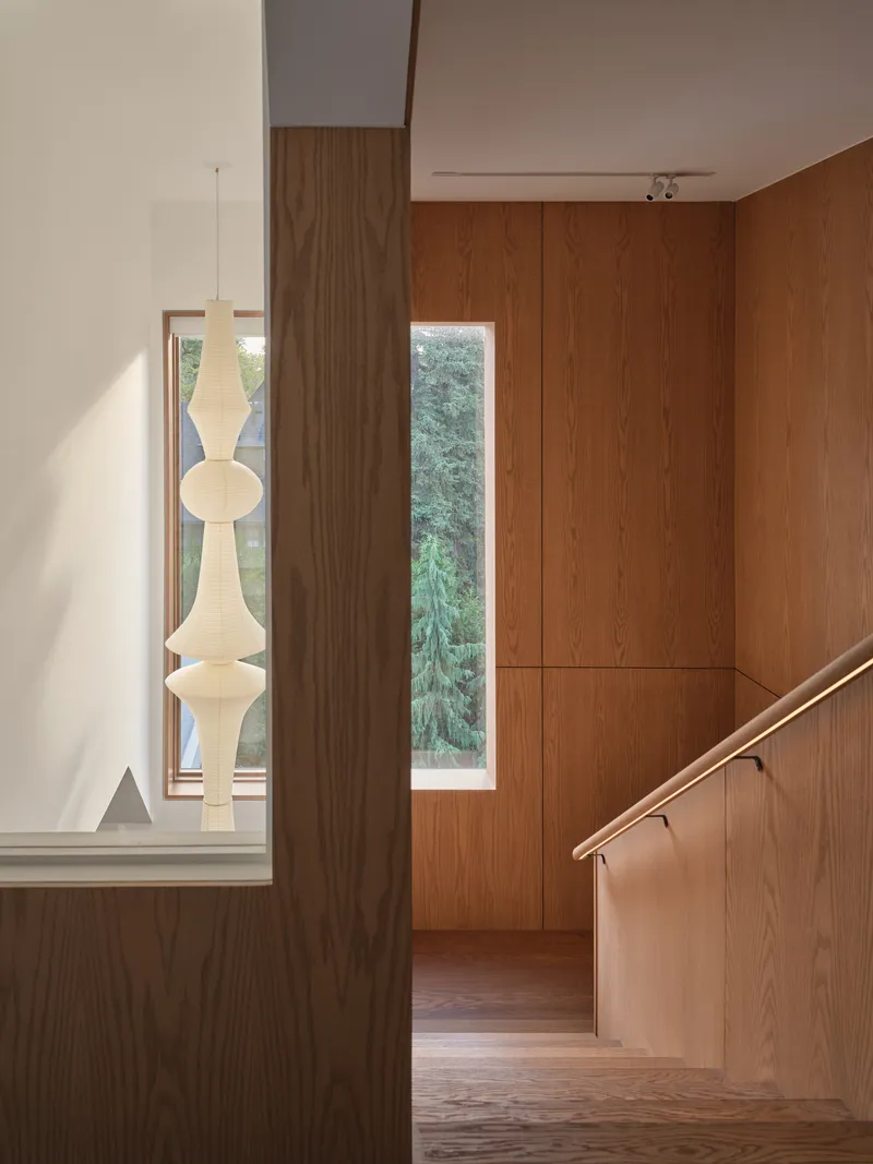 Upper hallway with vertical wood paneling and narrow window overlooking greenery