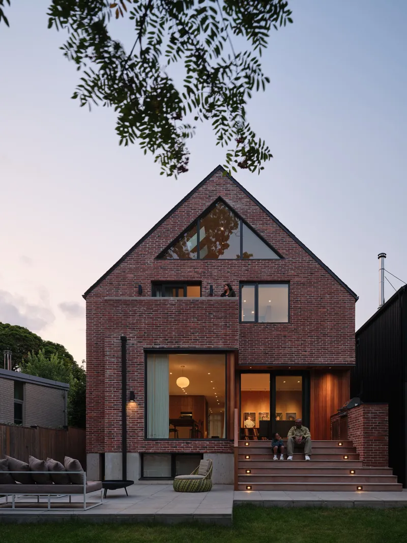 Red brick gable facade with glazed openings and timber deck at dusk