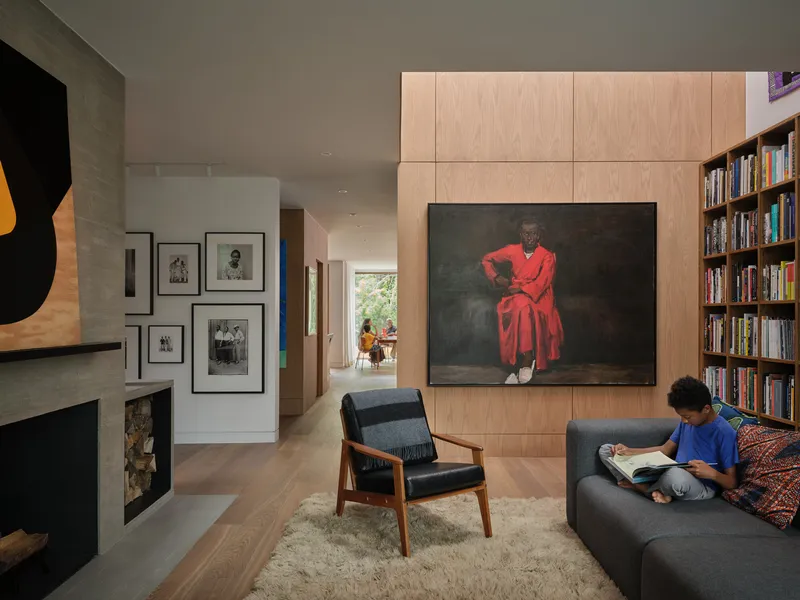 Living room with light wood cabinetry and built-in bookshelf, with a child reading on the sofa in afternoon light