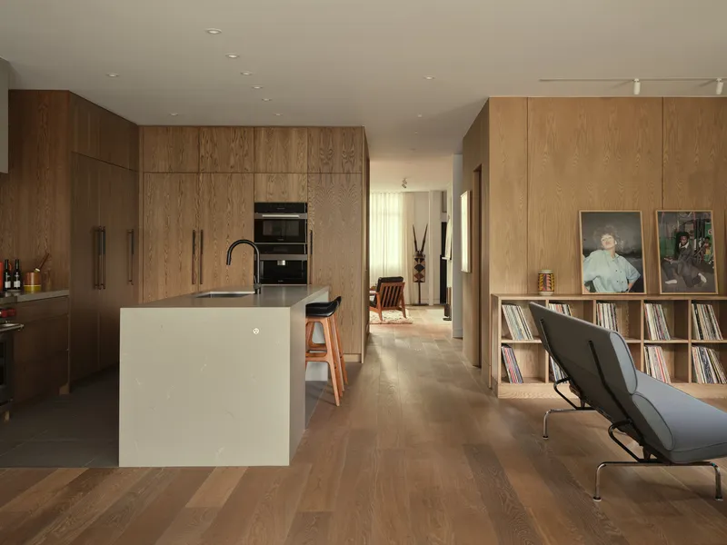 Open kitchen with white island and dark oak cabinetry, looking through to a corridor with vinyl storage