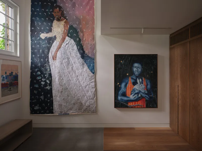 White gallery wall displaying two portrait paintings flanked by wood millwork and a window