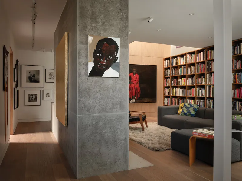 View through concrete column toward living area with floor-to-ceiling bookshelf in warm interior light