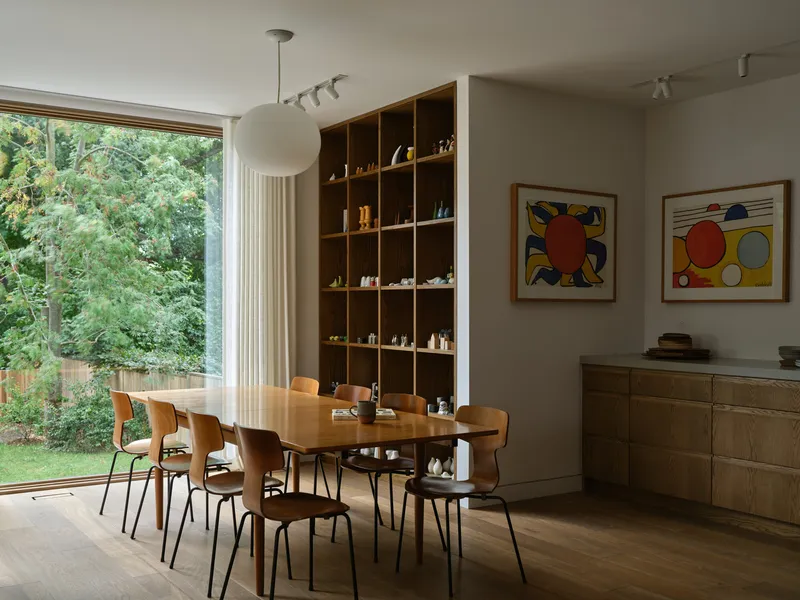 Dining room with oval table and plywood chairs overlooking green garden through full-height glazing